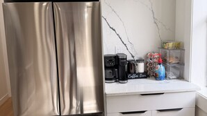 A modern kitchen with a stainless steel refrigerator, white cabinetry, and a marble backsplash.