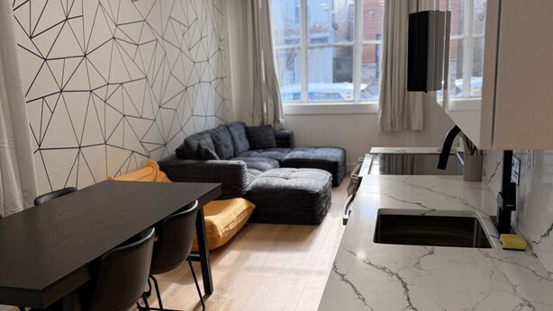 A modern kitchen with a marble countertop, a dining area with a dark table and chairs, and a cozy seating area with a sofa and cushions.
