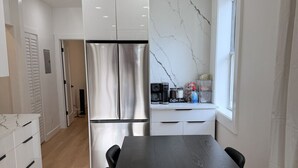 A modern kitchen with a large stainless steel refrigerator, white cabinets, and a marble backsplash.