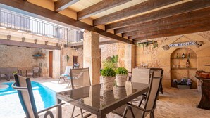 An outdoor dining area with a glass table and chairs, a pool, stone walls, and a bar area with a sign reading "CAS MERCADER". - CA'S MERCADER (ALGAIDA) - Beautiful rustic house with a private pool, perfect for cyclists (Algaida)