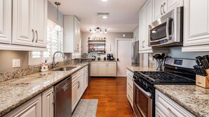 Una cocina moderna con armarios blancos, encimeras de granito, electrodomésticos de acero inoxidable y una isla central con asientos.