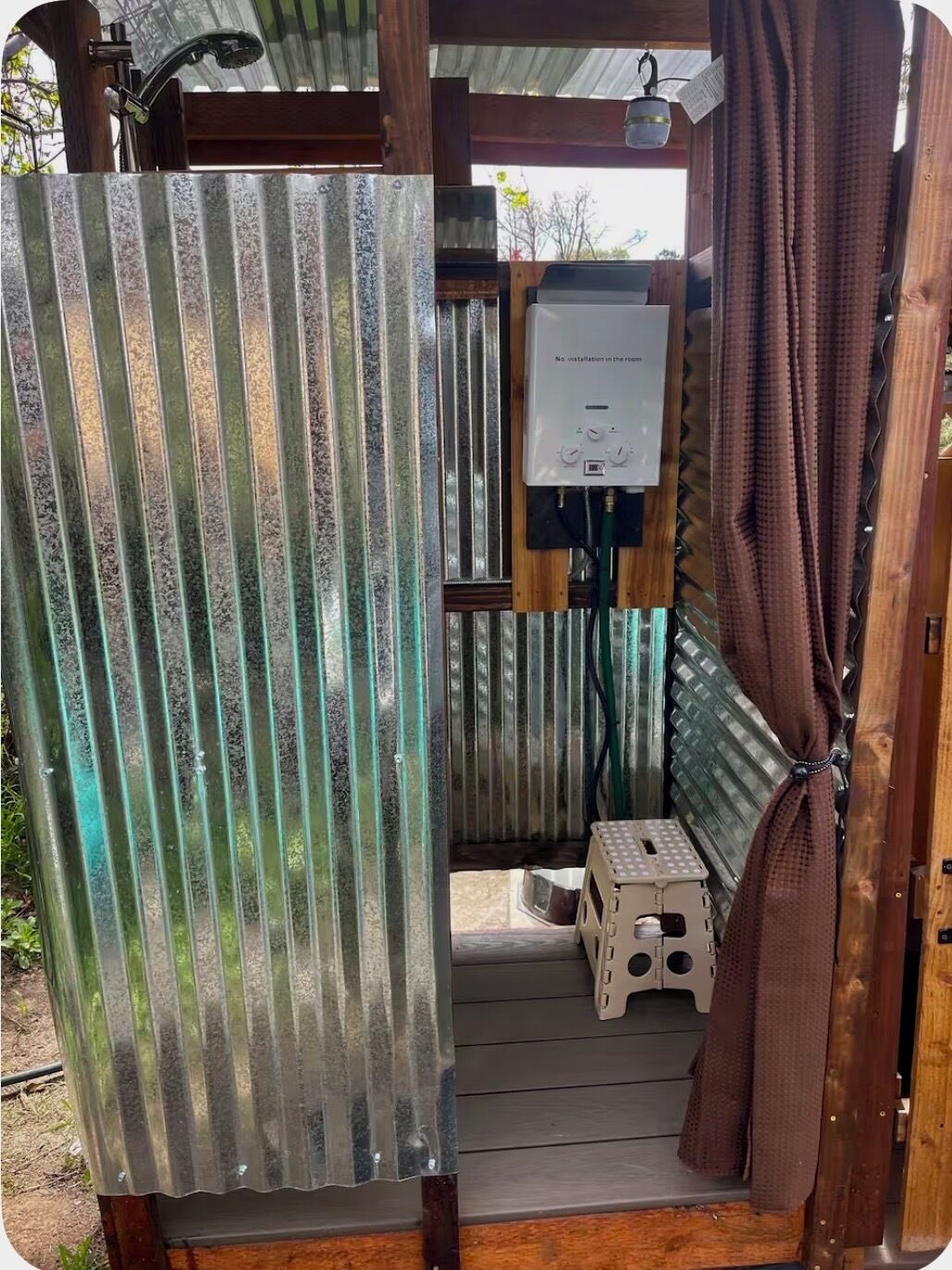 Een landelijke badkamer met een douche, toilet en een klein krukje.
