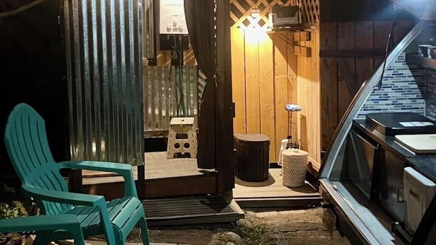 Un espace extérieur abrité, aménagé avec des chaises et une table, un véhicule et une structure en bois dotée d’une source de lumière.