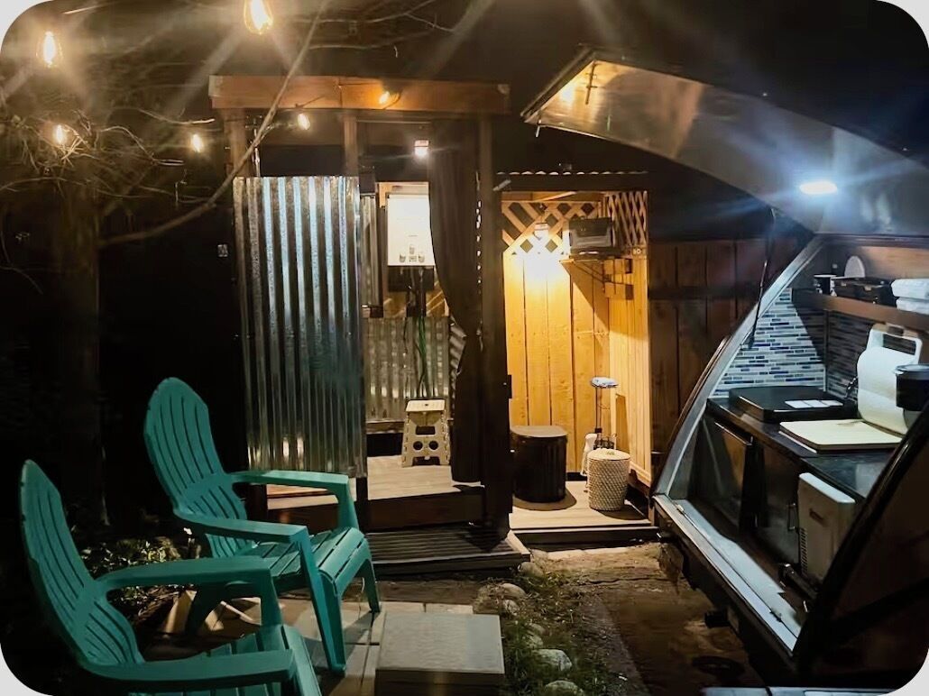 Eine Holzhütte mit überdachter Veranda, Sitzgelegenheiten im Freien und einem geparkten Fahrzeug.