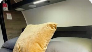 Un lit avec une couvre-lit matelassée grise et deux oreillers, un jaune et un blanc.