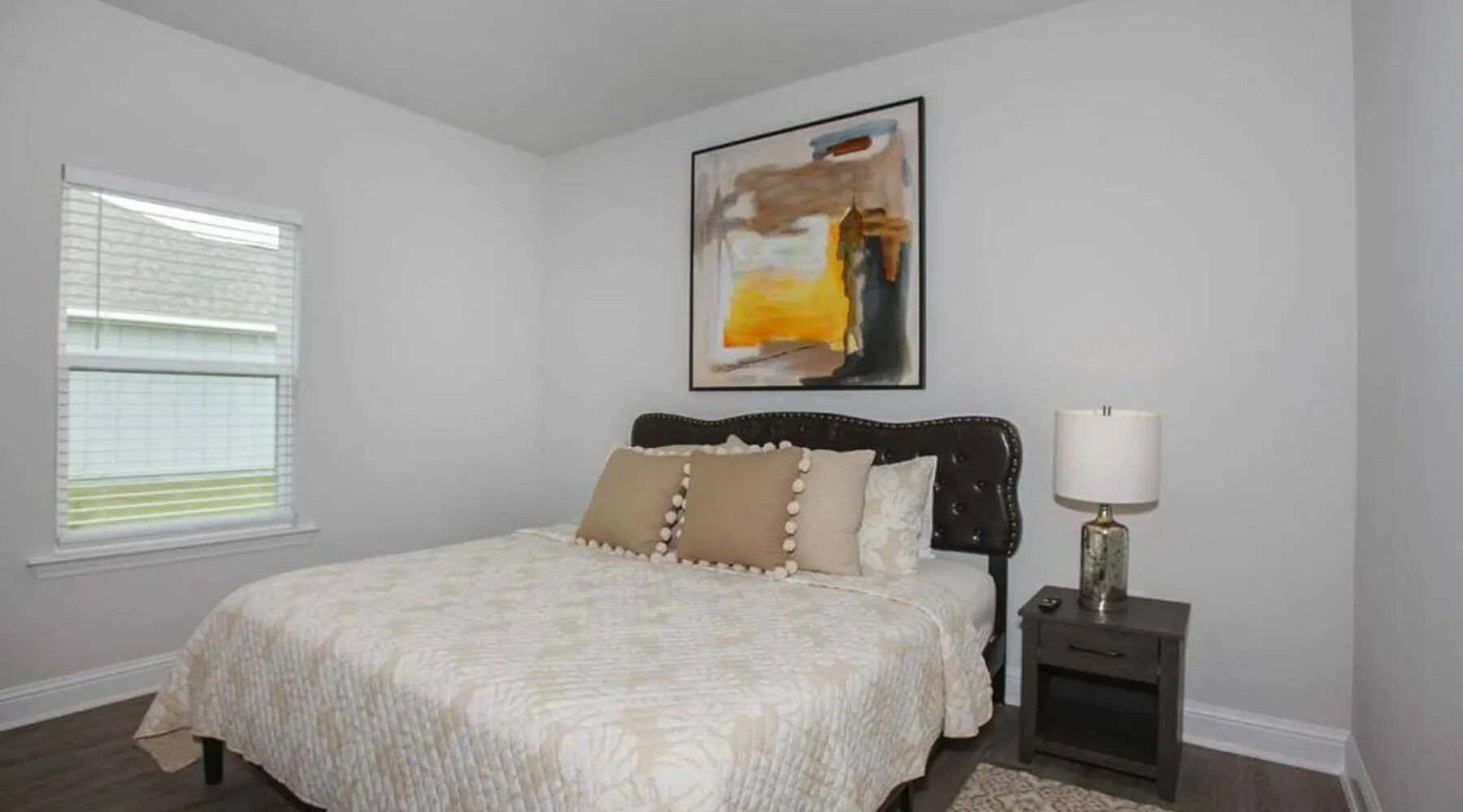 A bedroom with a bed, a nightstand, a lamp, and a window with blinds.