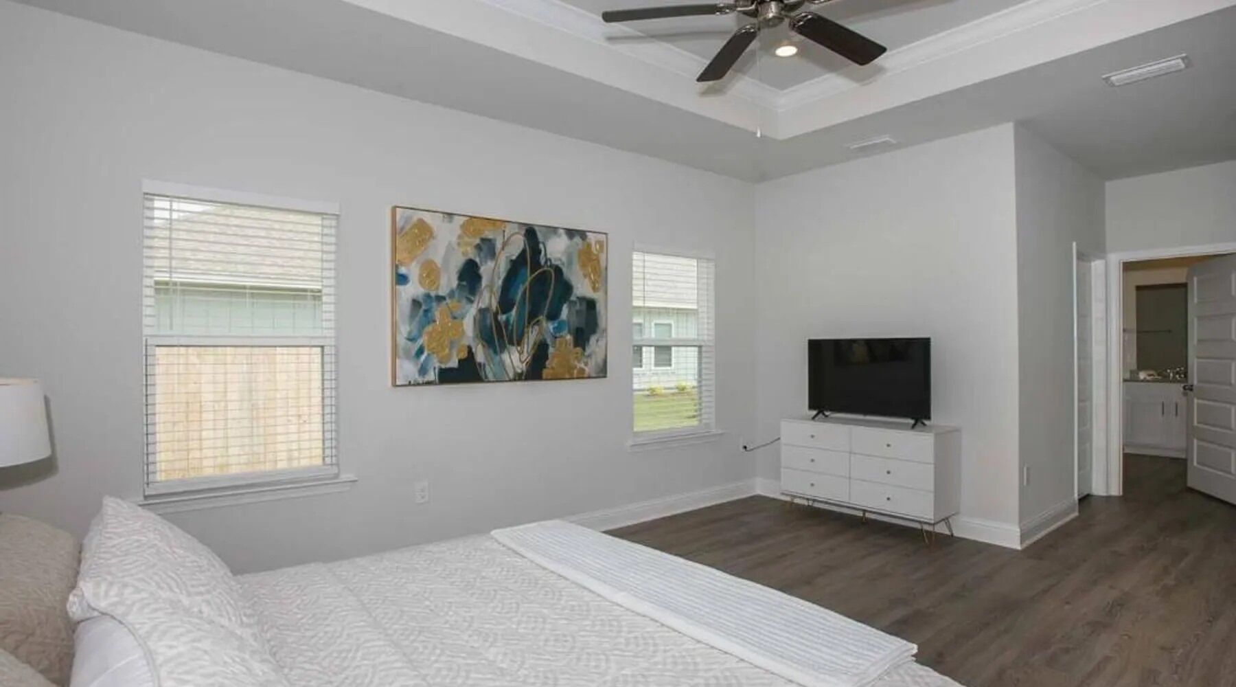 A bedroom with a bed, a TV on a dresser, and a ceiling fan.
