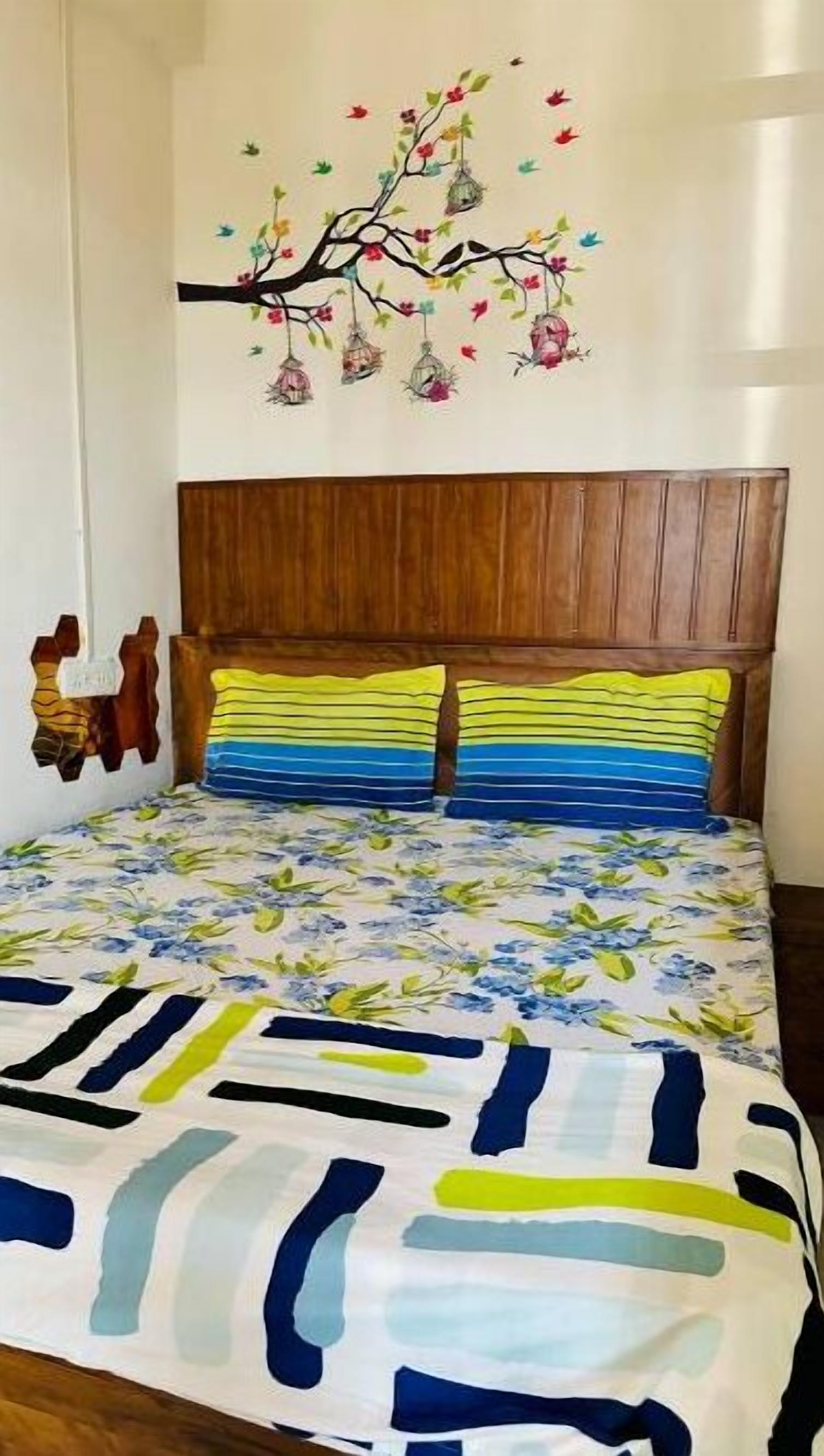 Un dormitorio con cabecera de madera, colcha estampada con flores y un mural de un árbol con casas de pájaros colgantes.