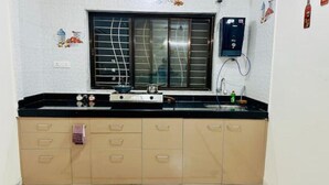 A kitchen with a gas stove, a sink, and a window with blinds. There is a wall-mounted electrical outlet and a small refrigerator.