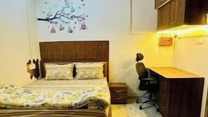 A bedroom with a bed, a desk, a chair, a ceiling fan, and a wall-mounted shelf.