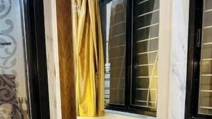 A corner room with a wooden cabinet, a mirror, and a window with a curtain.
