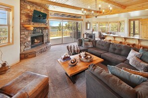 A cozy living room with a stone fireplace, a large sofa, and a wooden coffee table. - BIG Lake Views/AC/King Beds/Garage/Balconies/Games/Snow Summit, Marina, Village (Big Bear Lake)