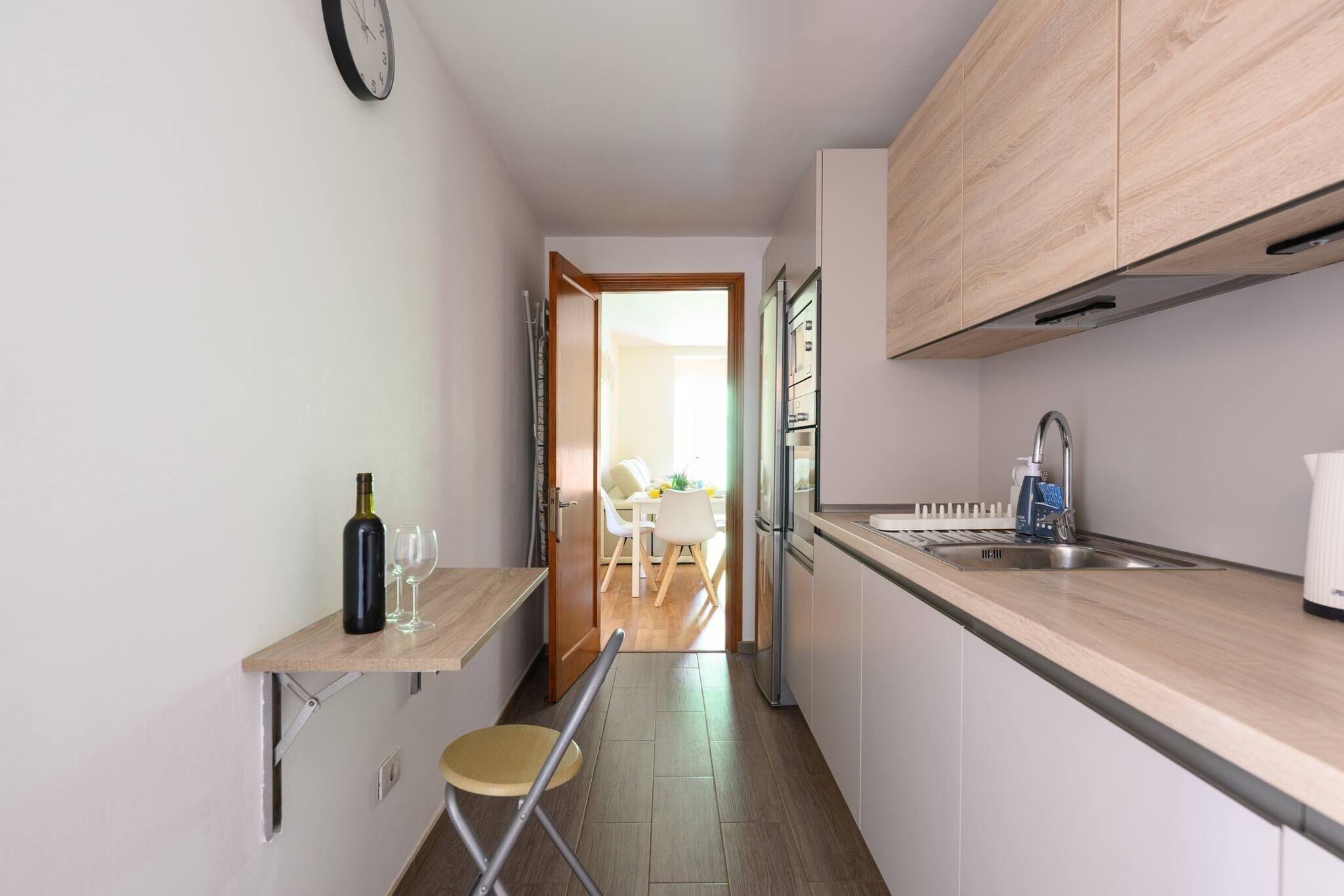 Een moderne keuken met een houten aanrecht, een inbouwgootsteen en een eethoek die zichtbaar is door een open deur.