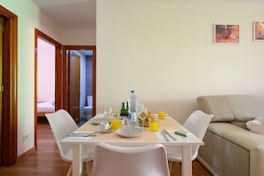 Een eetgedeelte met een tafel gedekt voor twee personen, een bank en een bed op de achtergrond.