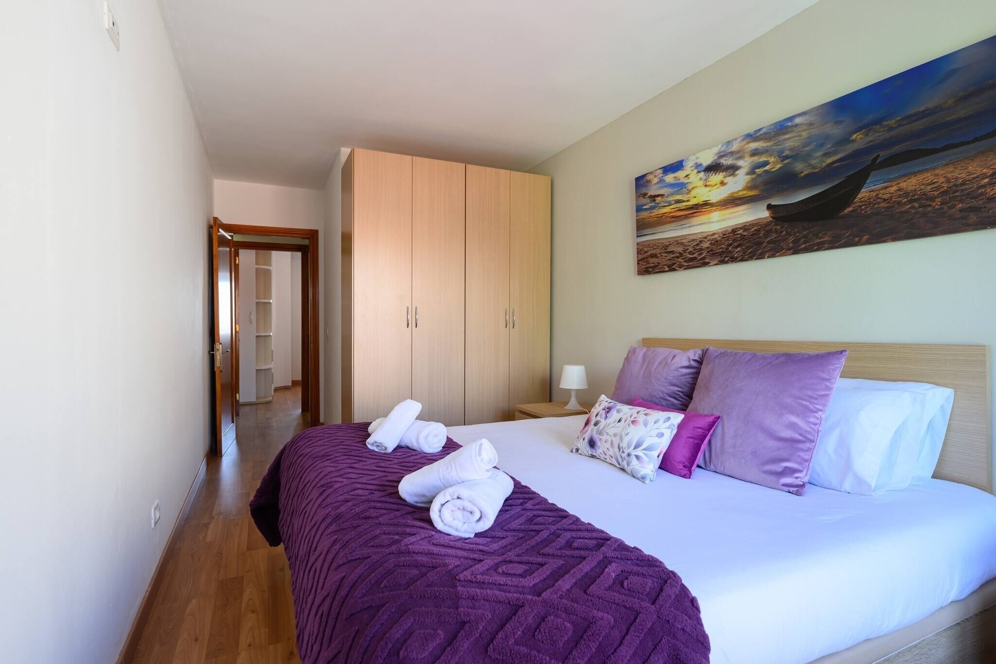 A hotel room with a bed, a wardrobe, a painting, and a hallway.