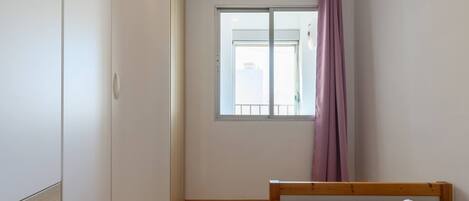 A room with a bed, a wardrobe, a window with a curtain, and a view of the outside.