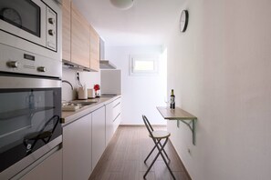 A compact kitchen with built-in appliances, a dining area with a chair, and a small window.