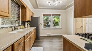 A kitchen with wooden cabinets, a granite countertop, a stainless steel refrigerator, and a window with a view of the outdoors.