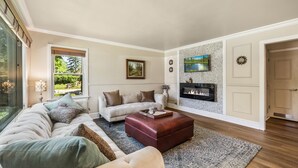 A spacious living room with a large sectional sofa, a red ottoman, and a fireplace.
