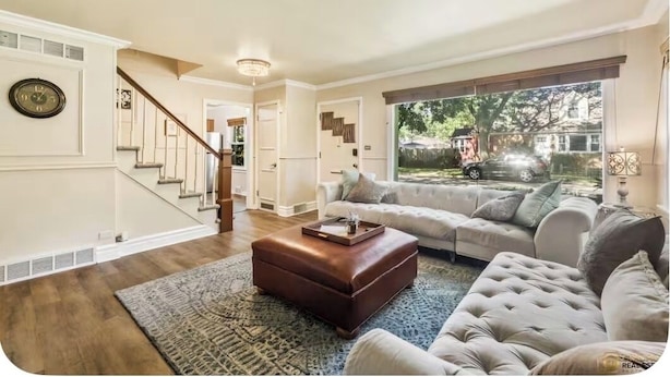 A spacious living room with a staircase, a large window with a view of the outdoors, and a cozy seating area with a leather ottoman and a tufted sofa.