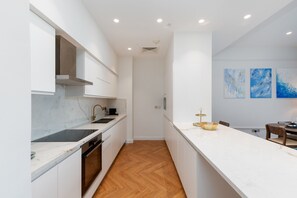 A modern kitchen with white cabinetry, a marble countertop, and a wooden floor. There are three blue abstract paintings on the wall.