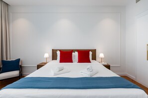 A hotel room with a large bed, two red pillows, white bedding, two bedside lamps, and a blue throw blanket.