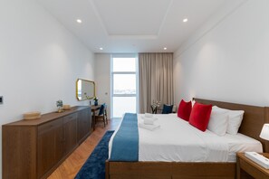 A modern hotel room with a large bed, a wooden desk, a mirror, and a view of the city.