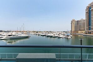 A marina with multiple yachts docked, a clear sky, and modern buildings in the background.