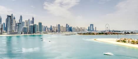 A coastal cityscape with modern skyscrapers, a sandy beach, and a clear blue sea.