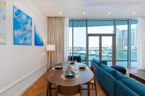 A modern dining area with a round table set for four, a sofa, and a view of a marina through large windows.