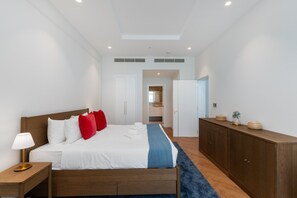 Une chambre d’hôtel moderne, dotée d’un grand lit, d’une table de chevet, d’une armoire et d’une salle de bain visible à travers une porte ouverte.