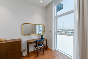 Una habitación con escritorio de madera, una silla, un espejo y vista a un puerto deportivo a través de un ventanal grande.
