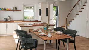 A modern kitchen with white cabinets, a wooden dining table set for four, and a staircase leading to an upper level.
