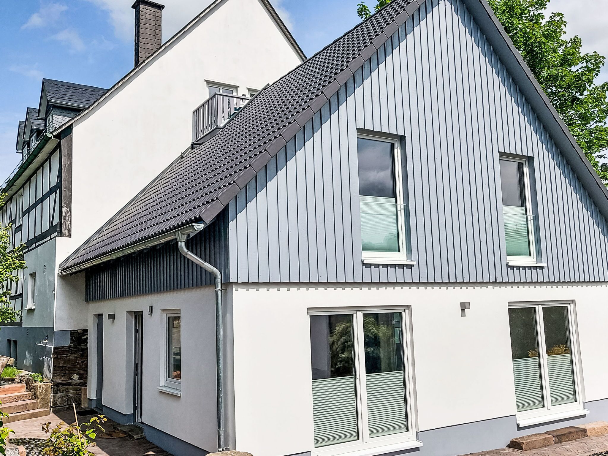 A modern two-story house with a sloped roof, large windows, and a visible chimney.