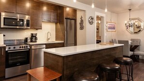 A modern kitchen with stainless steel appliances, a central island with stools, and a dining area with a chandelier.