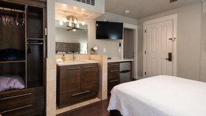 A bedroom with a bed, a vanity with a mirror, a television, and a wardrobe.
