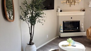 Una sala de estar con chimenea, televisor y una planta grande.