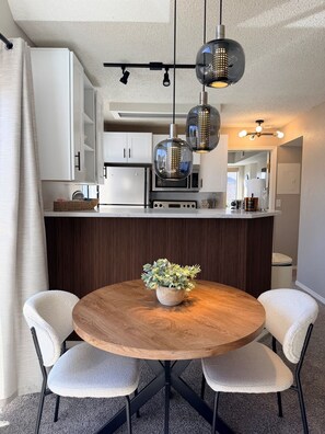 A modern kitchen with white cabinets, a wooden island, and a round dining table with two chairs.