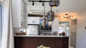 Una cocina moderna con armarios blancos, un microondas y un comedor con una mesa redonda de madera y dos sillas.