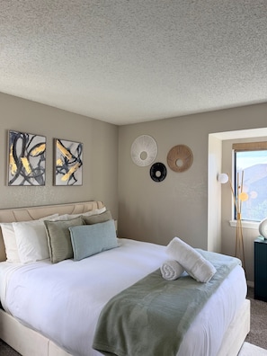 A bedroom with a bed, pillows, wall art, and a window.