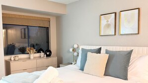 Una cama bien hecha con almohadas, una mesita de noche con lámpara y dos cuadros en la pared.