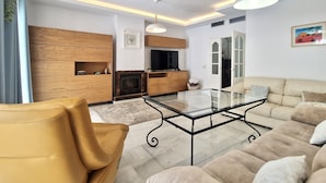 A modern living room with a sofa, a glass coffee table, and a wooden entertainment unit. - SR Torremar beautiful villa with garden (Marbella)