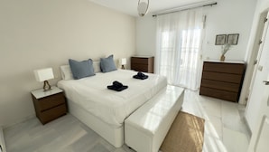 A modern bedroom with a large bed, bedside tables, a dresser, and a window with sheer curtains. - SR Torremar beautiful villa with garden (Marbella)