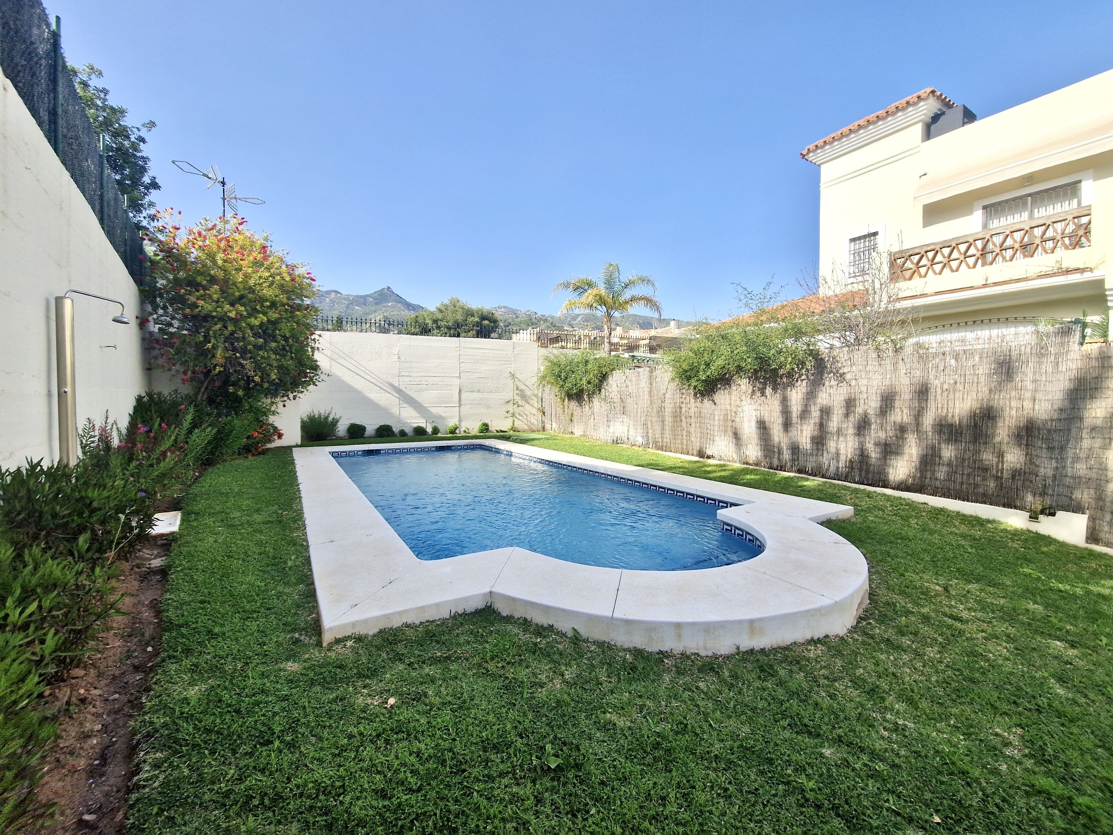 A swimming pool with a unique shape, surrounded by well-maintained grass and a wooden fence.