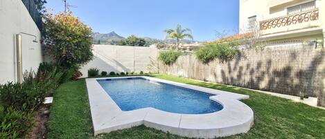 A swimming pool with a unique shape, surrounded by well-maintained grass and a wooden fence.