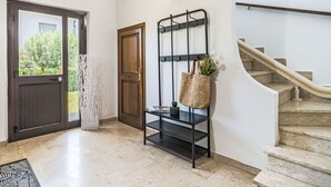 Um corredor com uma porta de madeira, uma estante de metal preto com uma sacola trançada e uma escadaria de mármore.