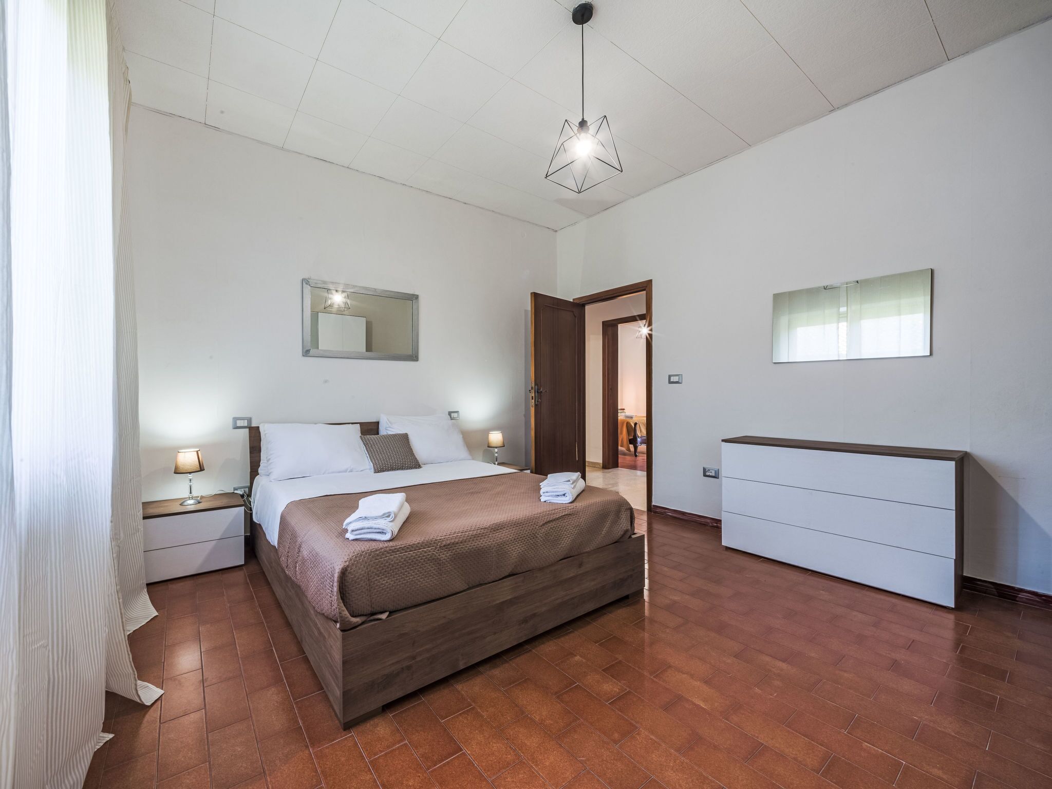 Une chambre à coucher comprenant un lit, des tables de chevet, une commode, un miroir et un luminaire suspendu.