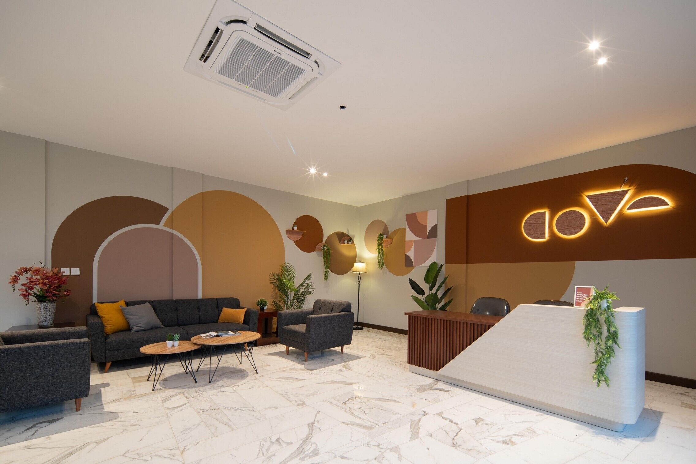 Un área de recepción moderna con suelo de mármol, un sofá, una mesa de centro y un mostrador de recepción con una planta.