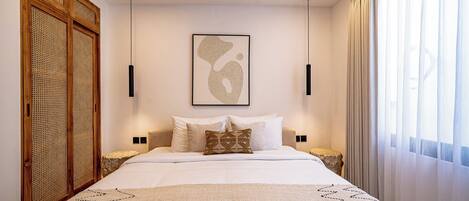 A neatly arranged bedroom with a large bed, a wooden wardrobe, and a framed artwork on the wall.