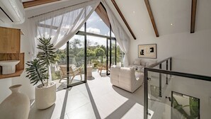 A spacious living room with a large glass door leading to a balcony, a white sofa, and a potted plant.